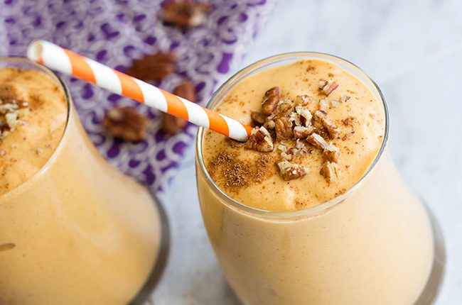 Side image of 2 curved glasses filled with pumpkin smoothie topped with cinnamon and pecans