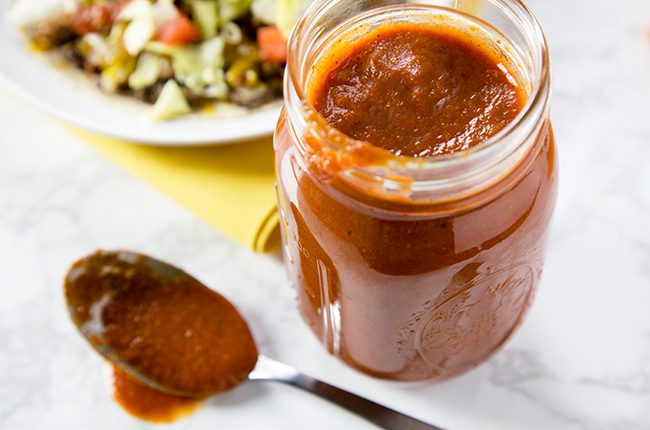 Red Enchilada Sauce in a glass jar with a spoon beside jar