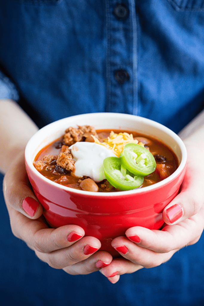 Red bowl of turkey chili being held by a woman wearing blue