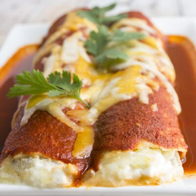 Square image of cheese enchiladas on white plate ready to serve