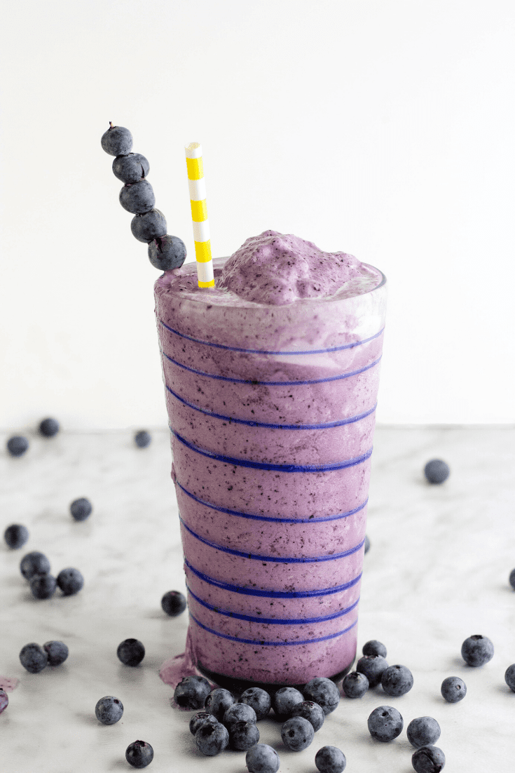 Tall glass with blue piping filled with blueberry smoothie and yellow paper straw