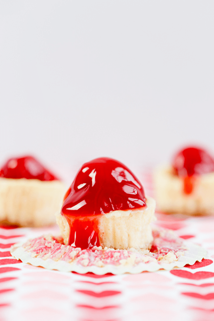 Three mini cheesecakes on a red and white cloth topped with cherry pie filling