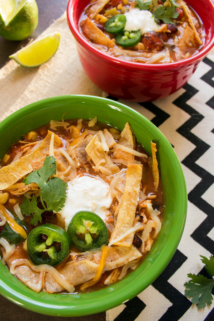 Two bowls of chicken tortilla soup on a counter topped with tortilla strips and jalapeno