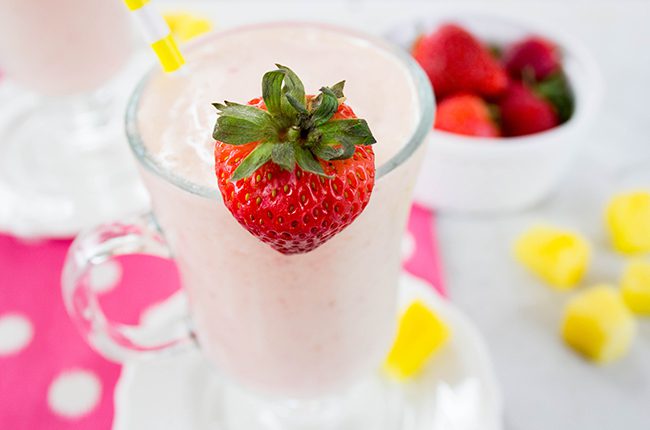 Up close picture of a strawberry pineapple smoothie in a tall glass with strawberry garnish