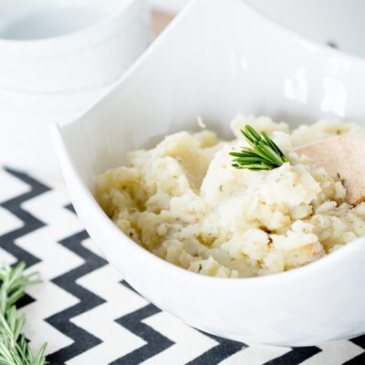 White bowl filled with parsnip mash with sprig of rosemary