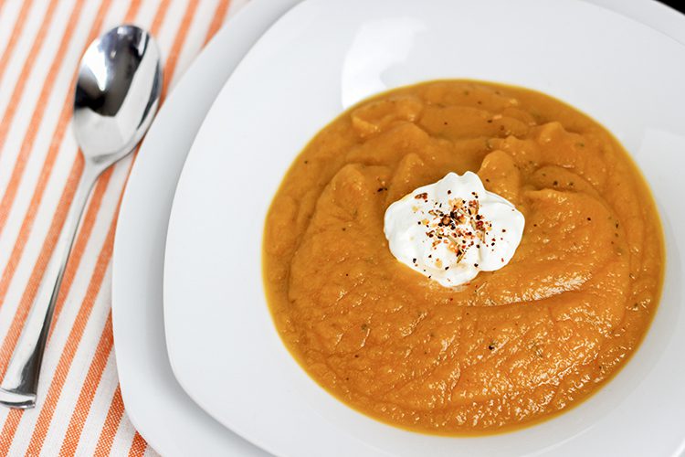 White bowl of squash soup laying on orange and whit striped cloth napkin