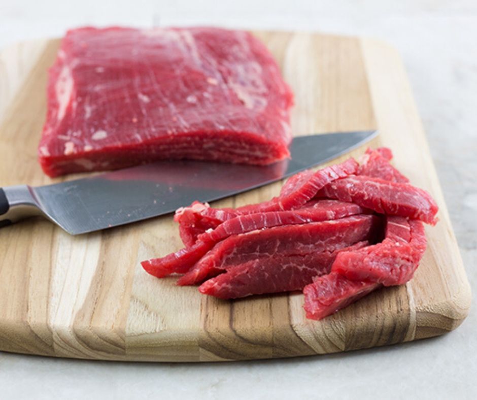 Flank steak on a cutting board being sliced for beef stir fry recipe