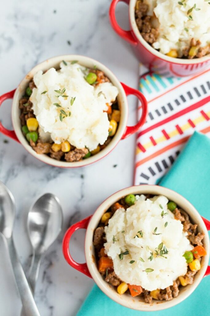 Overhead picture of mini shepherds pies in small red mugs laying on a marble counter