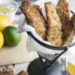 Tilapia fish sticks on a white plate with tartar sauce and lemon slices