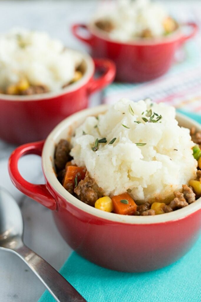 Up close picture of the best shepherds pie in a small red bowl topped with light mashed potatoes