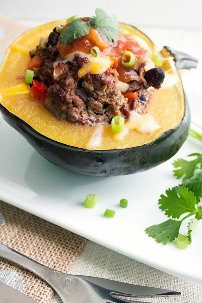 Up close stuffed acorn squash on white plate with cheese and salsa