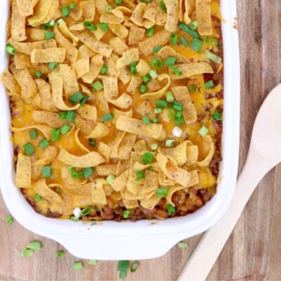 frito pie close up topped with fritos and green onions in a white casserole dish