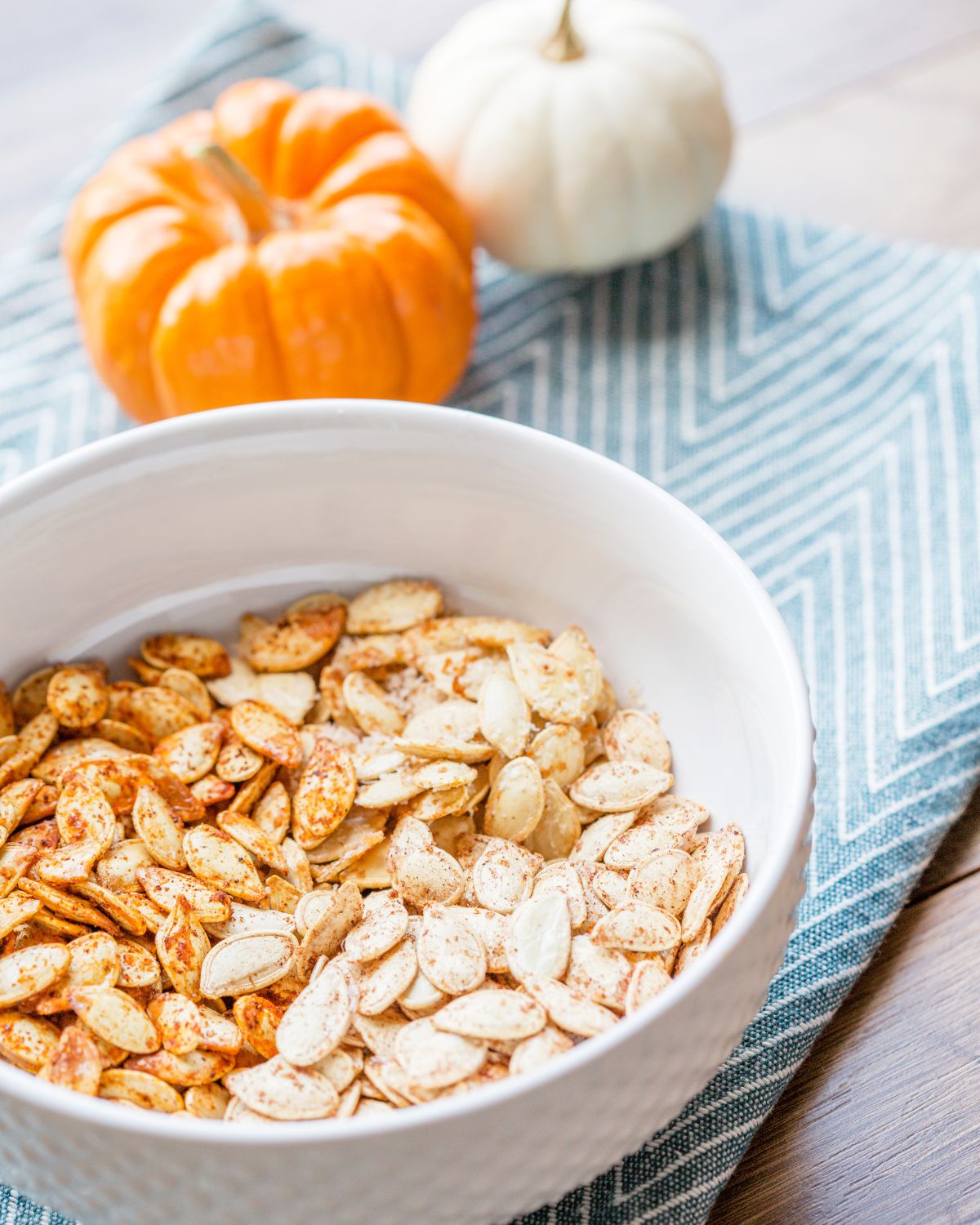 Large white bowl filled with two flavors of roasted pumpkin seeds sitting on a blue napkin